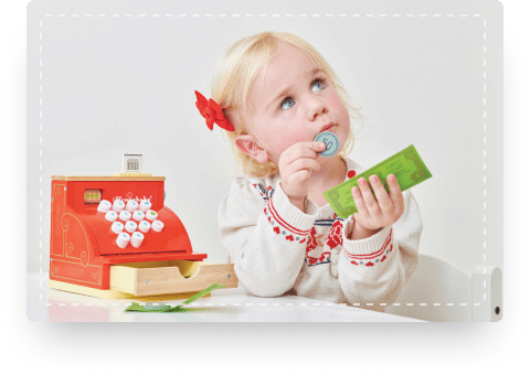 Little girl plays shop keeper with a wooden toy till and pretend money