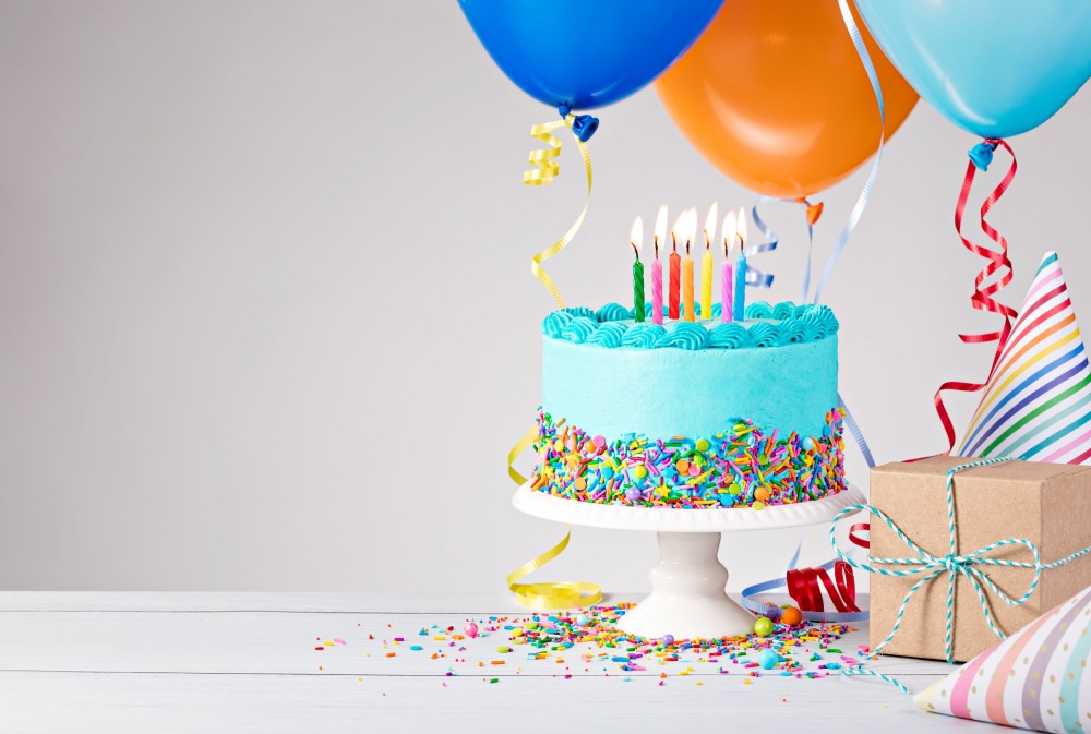 Birthday cake with candles and balloons, with gift wrapped toys for children